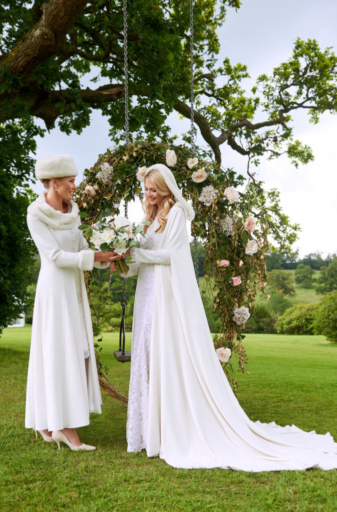 Mother of the bride holds hands with bride both wearing vory