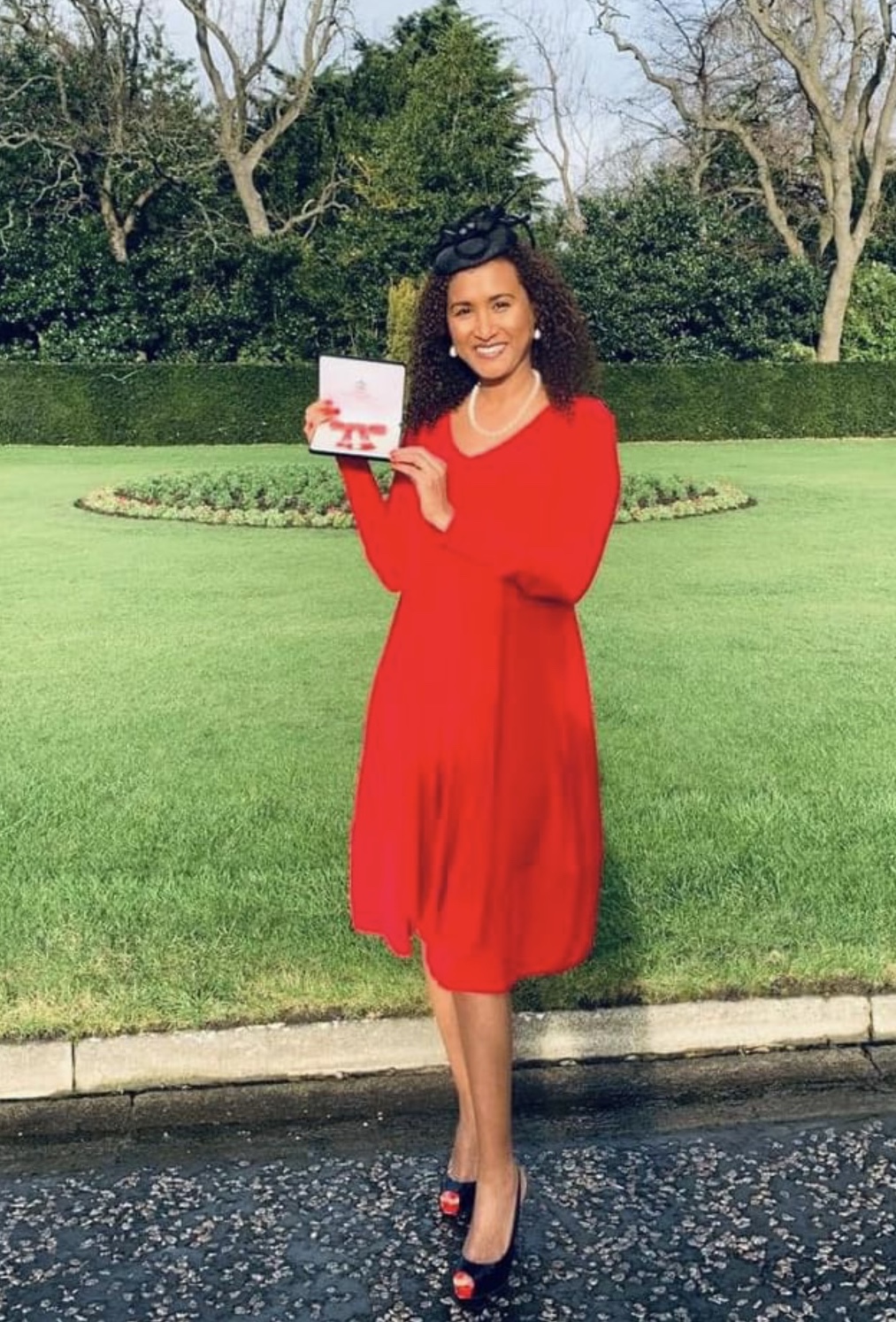 Woman in red holds up MBE award to photographer at Holyrood Castle