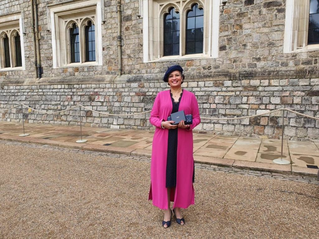 Lady in pink holds up her award outside Windsor Castle