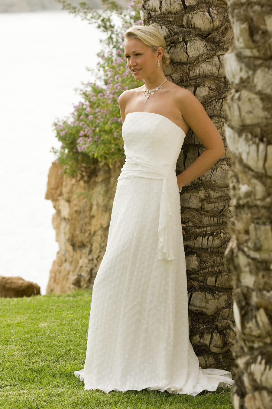 Model leaning against a stone wall in long ivory wedding dress at beach wedding
