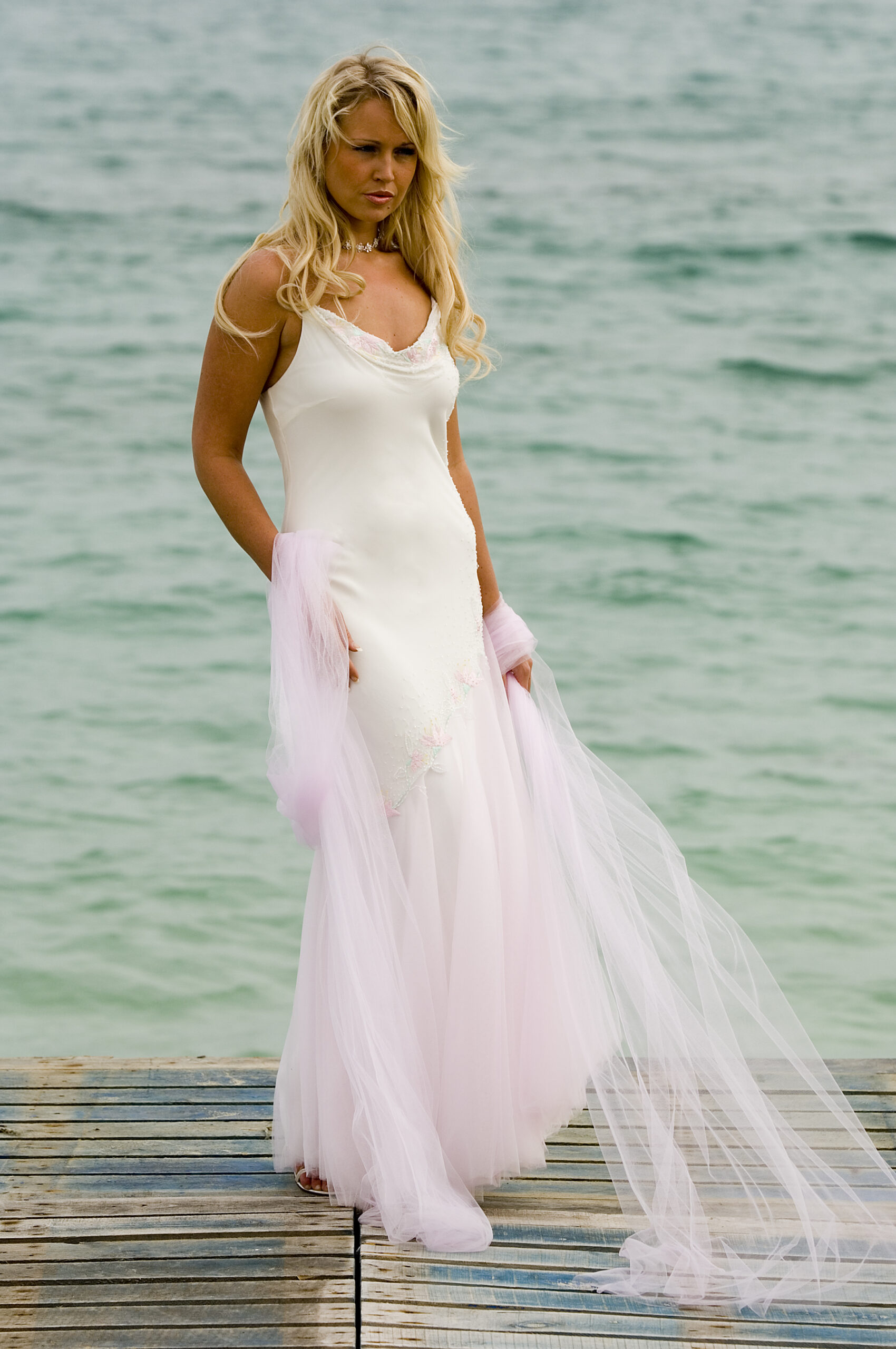 honeymoon dress ivory and blush pink embellished wedding bridal dress. Bride wearing dress standing on sandy beach infront of sea on wedding day.