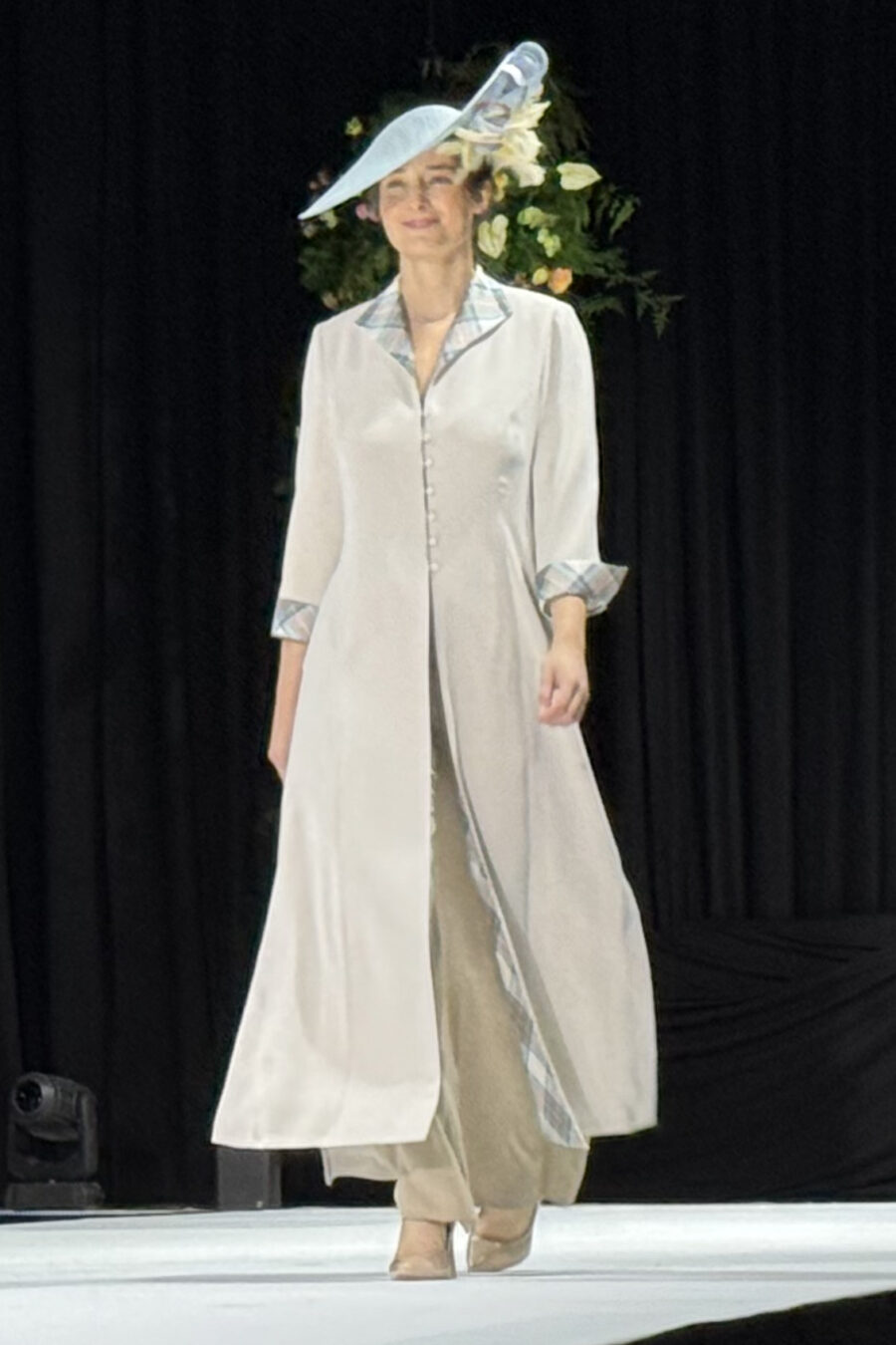 Model on catwalk wearing long silk coat with tartan collar and cuffs coordinaling